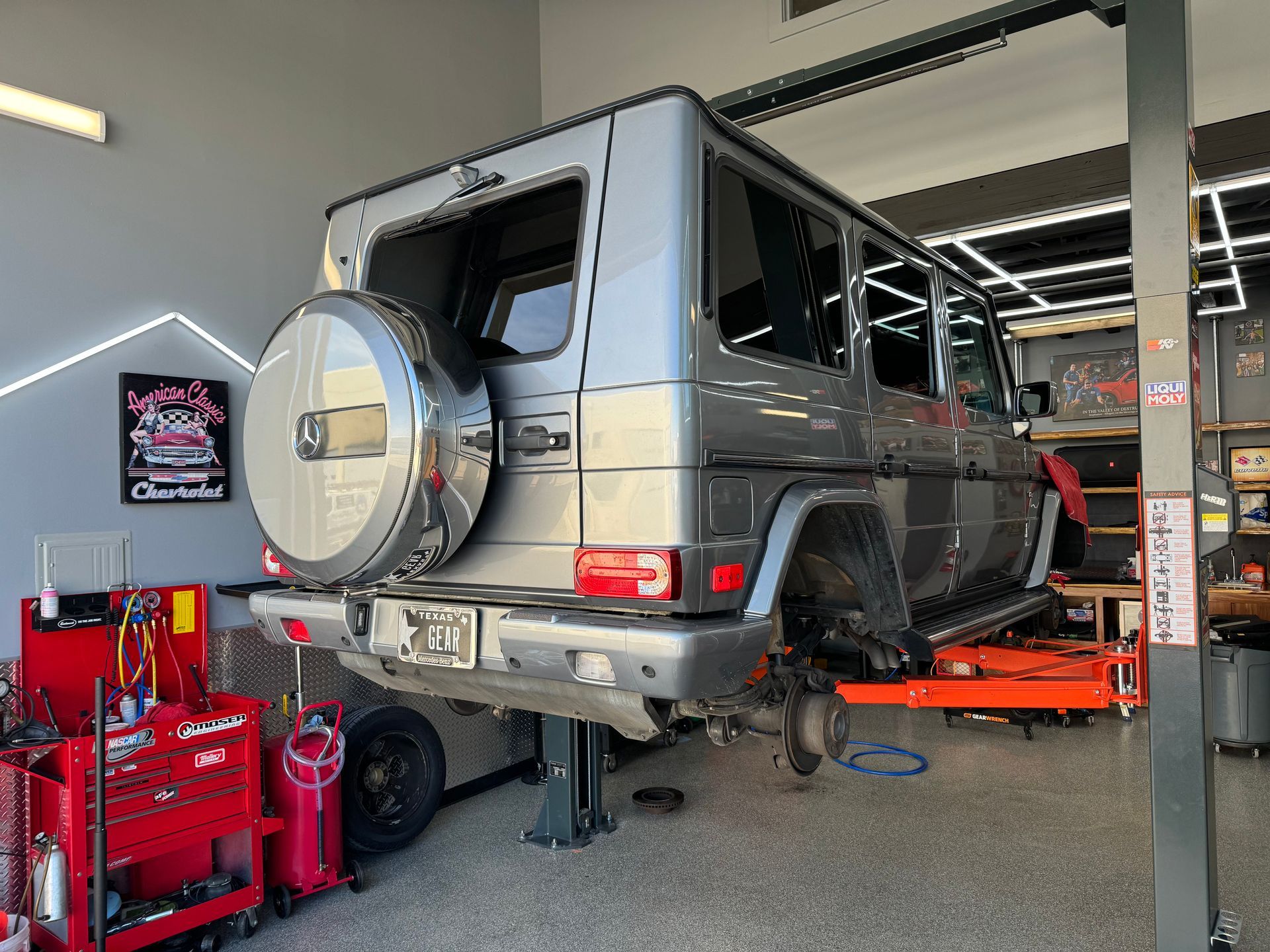 A gray Mercedes-Benz G-Wagon raised in a garage, rear wheels removed, being worked on. | Auto Motive