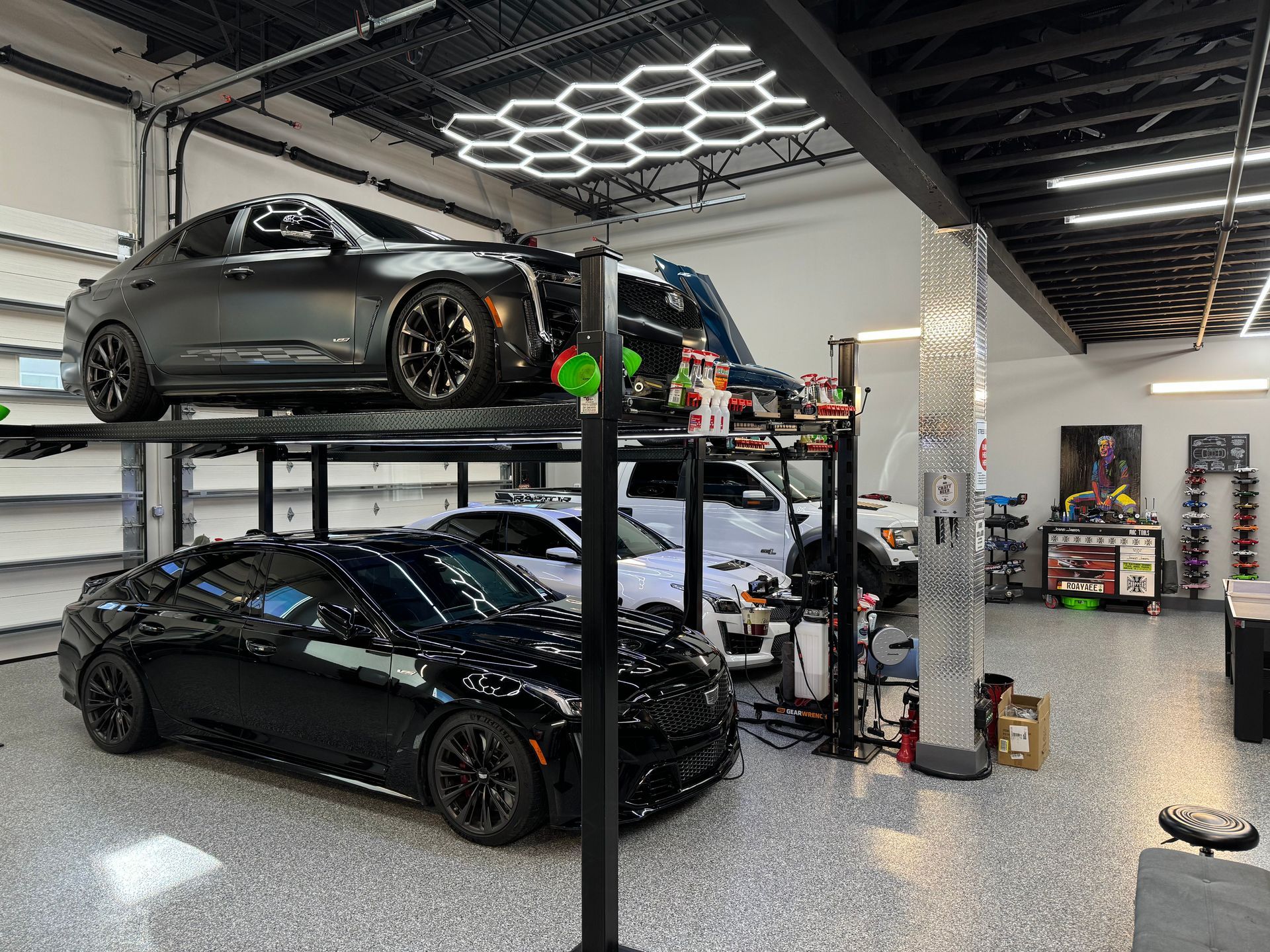 Cars on a two-post lift inside a well-lit garage with hexagon ceiling lights.v