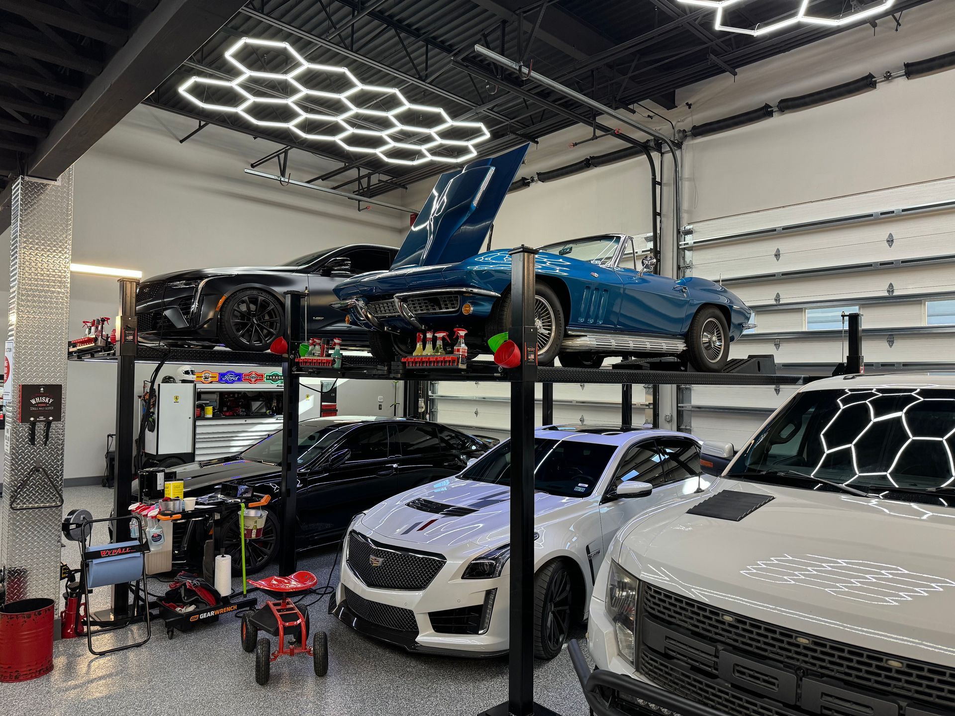 Cars in a well-lit garage with lifts. Two classic cars are on the upper level. | Auto Motive