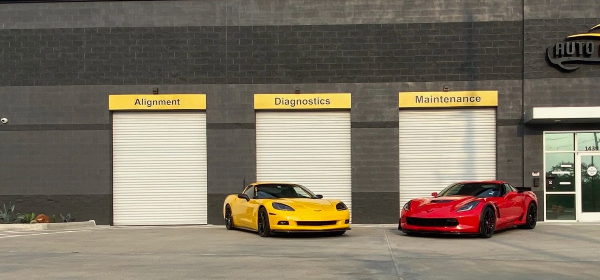 Two Corvette sports cars, yellow and red, parked in front of a garage. | Auto Motive