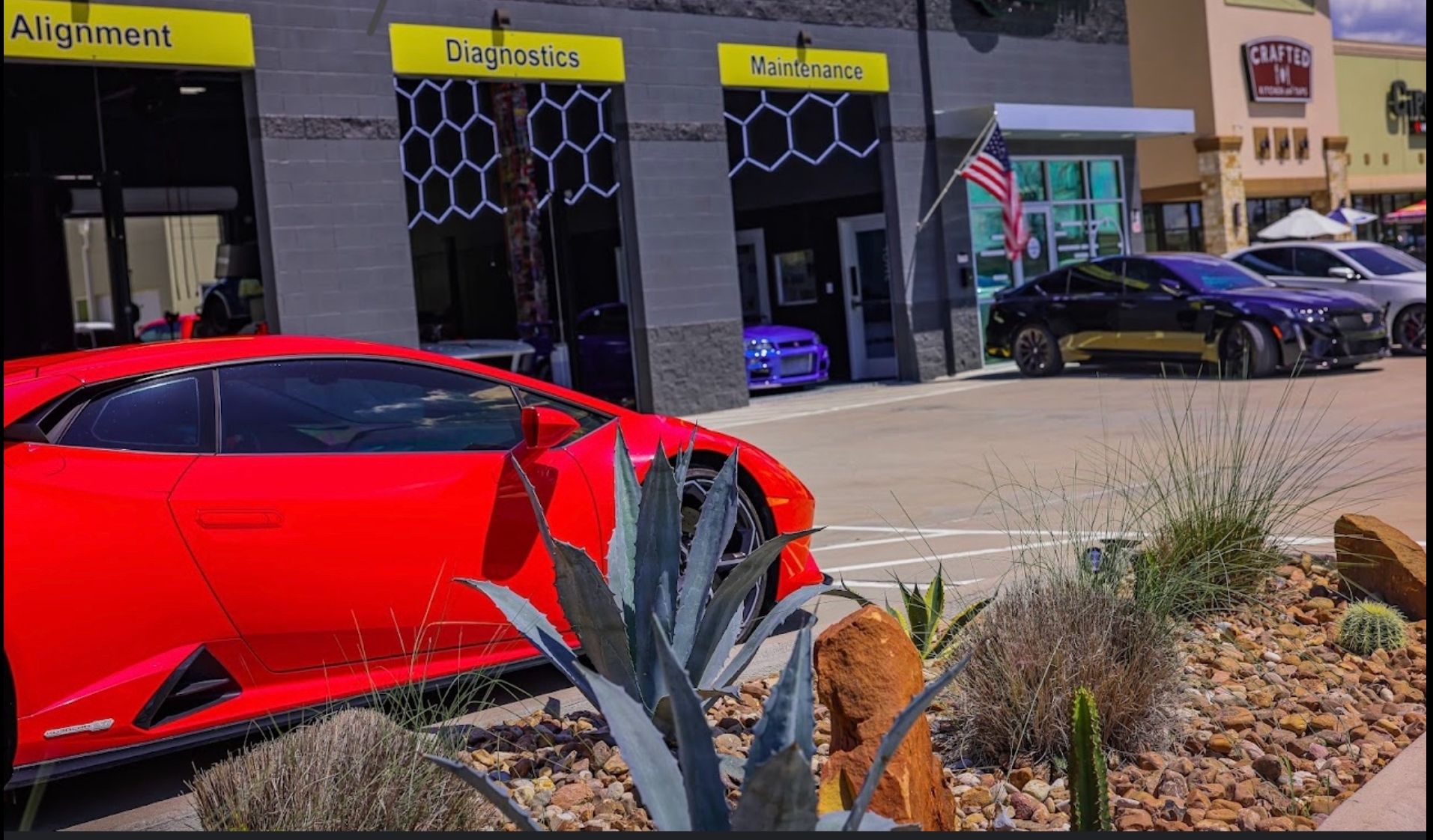 Red sports car parked in front of a car repair shop; other cars visible; desert landscaping. | Auto Motive