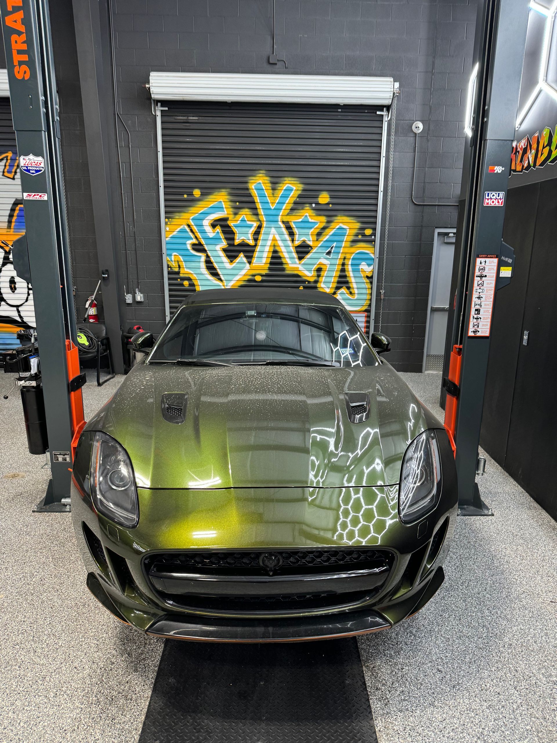 Green Jaguar sports car inside a garage with graffiti and a closed garage door. | Auto Motive