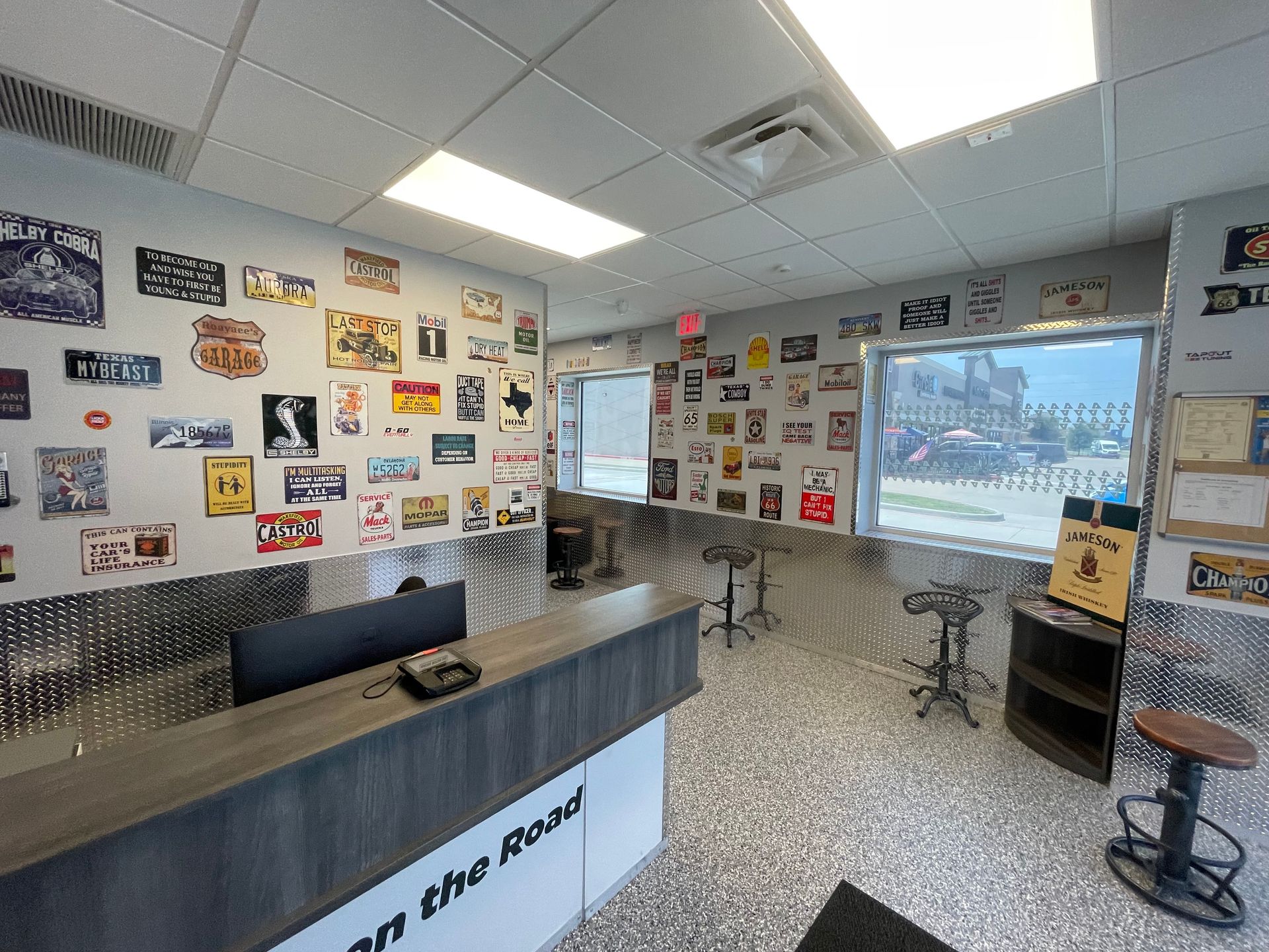 Reception area with road signs on walls. Gray countertop, diamond-pattern metal walls, stools, and large window. | Auto Motive