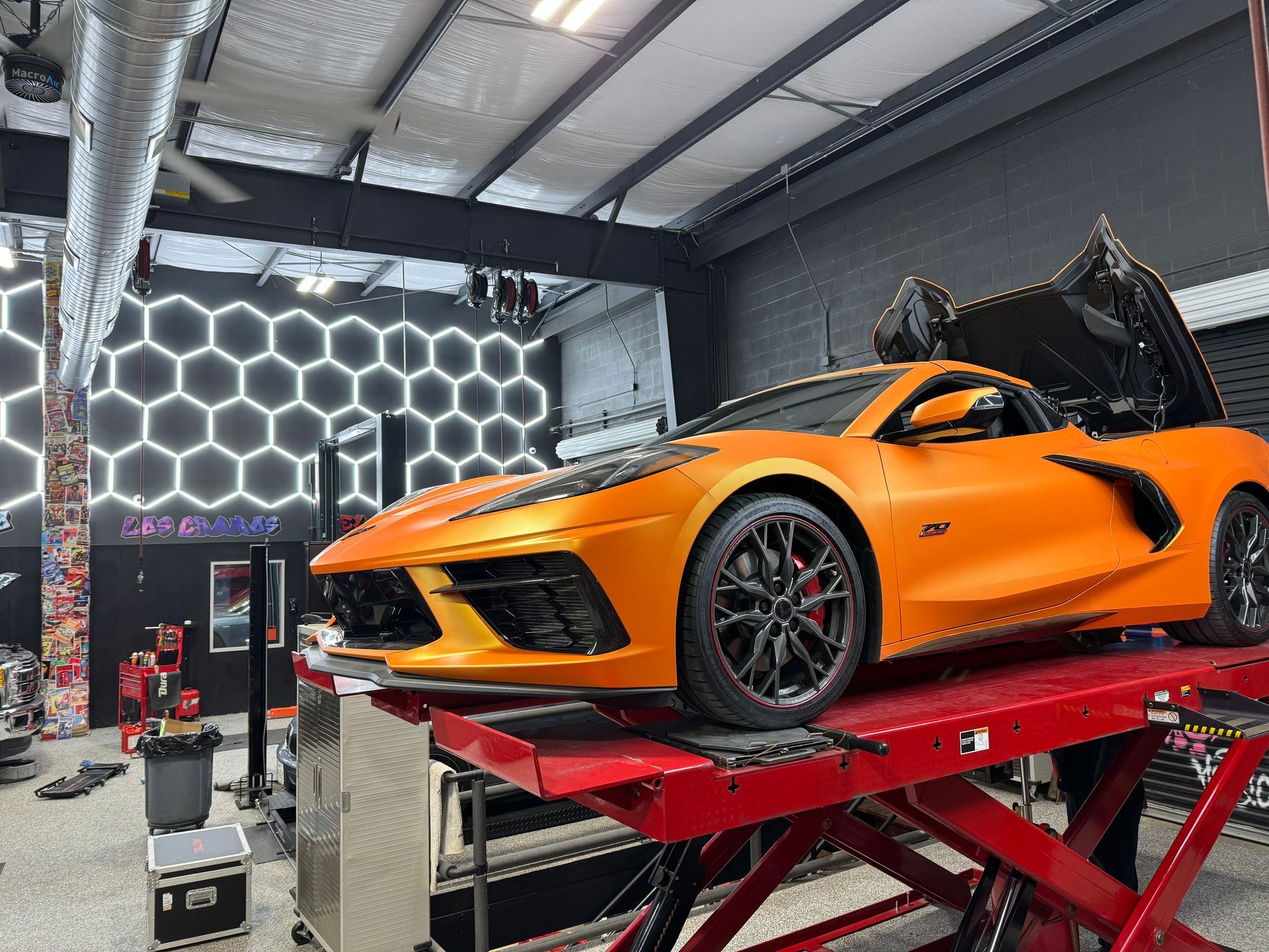 Orange Corvette on a red lift inside a shop with hexagon lights. | Auto Motive
