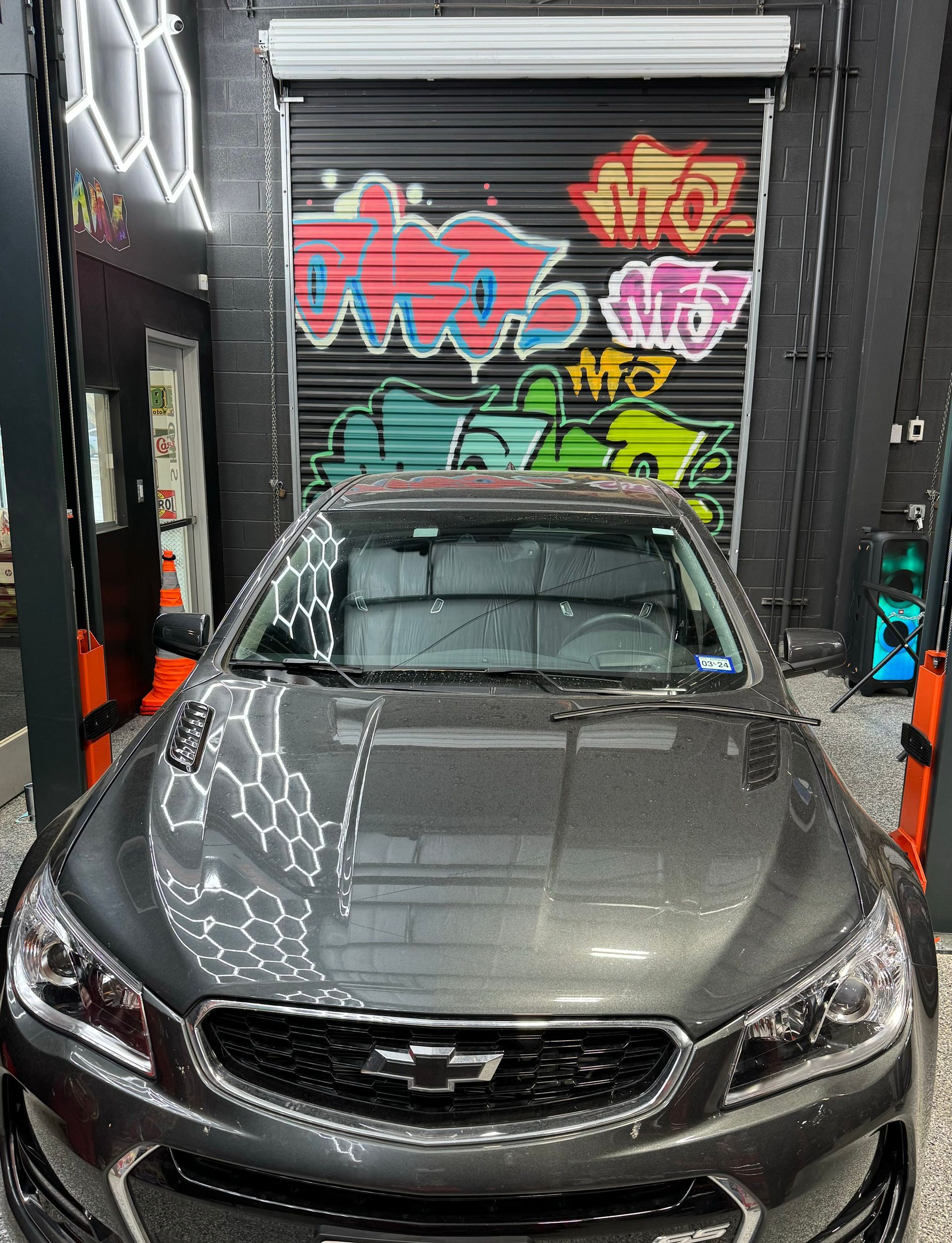 Gray Chevrolet SS in a garage with graffiti-covered door; hexagon-lighted wall. | Auto Motive