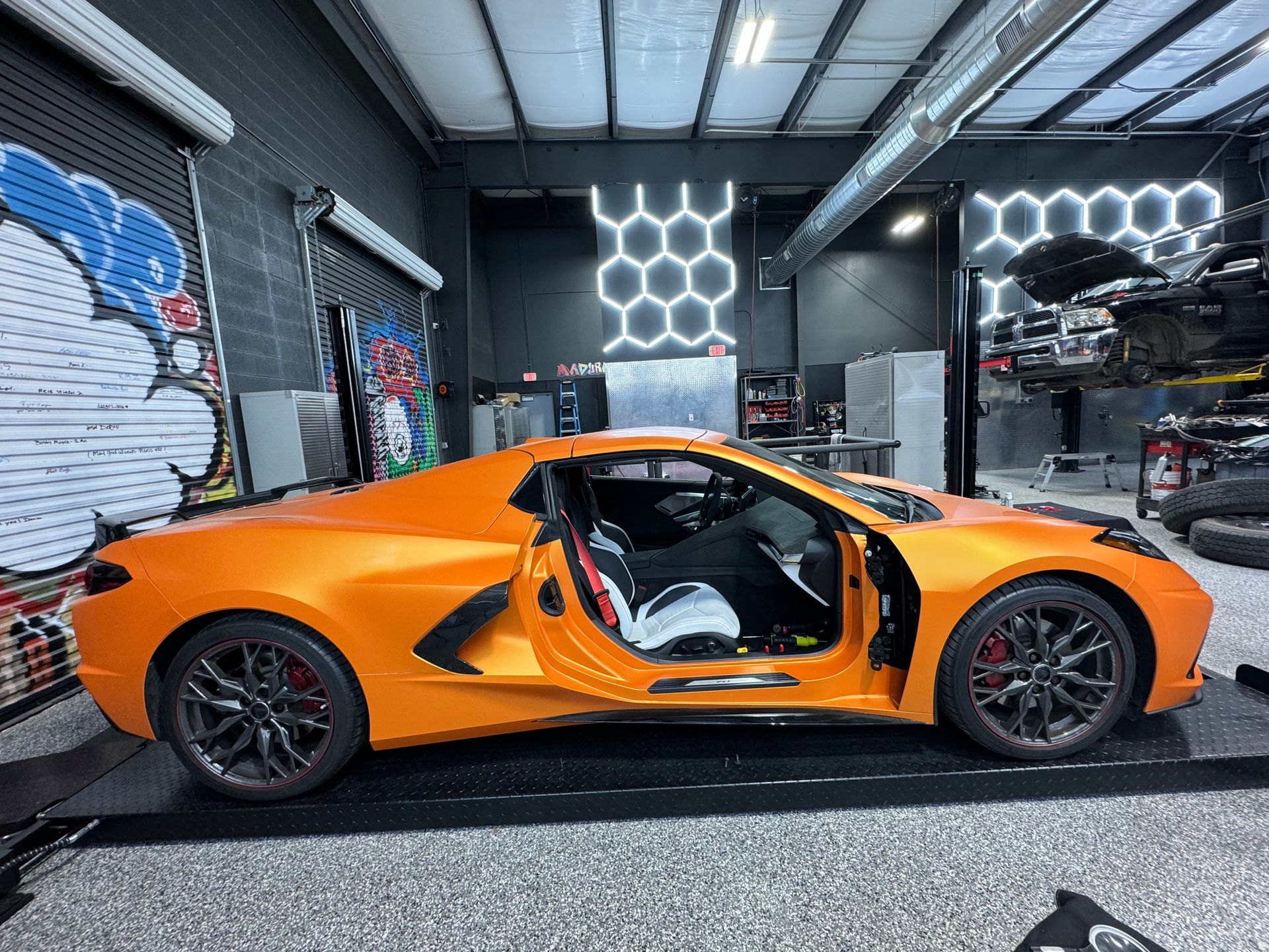 Bright orange sports car with door open in a garage. Red brake calipers, black wheels. | Auto Motive