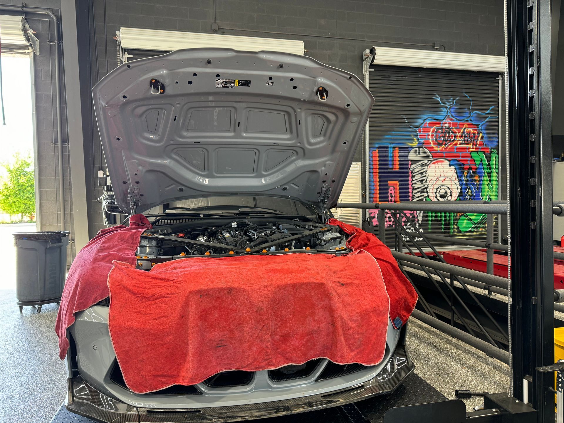 A gray car with the hood open inside an auto shop; a red cover protects the front end. | Auto Motive