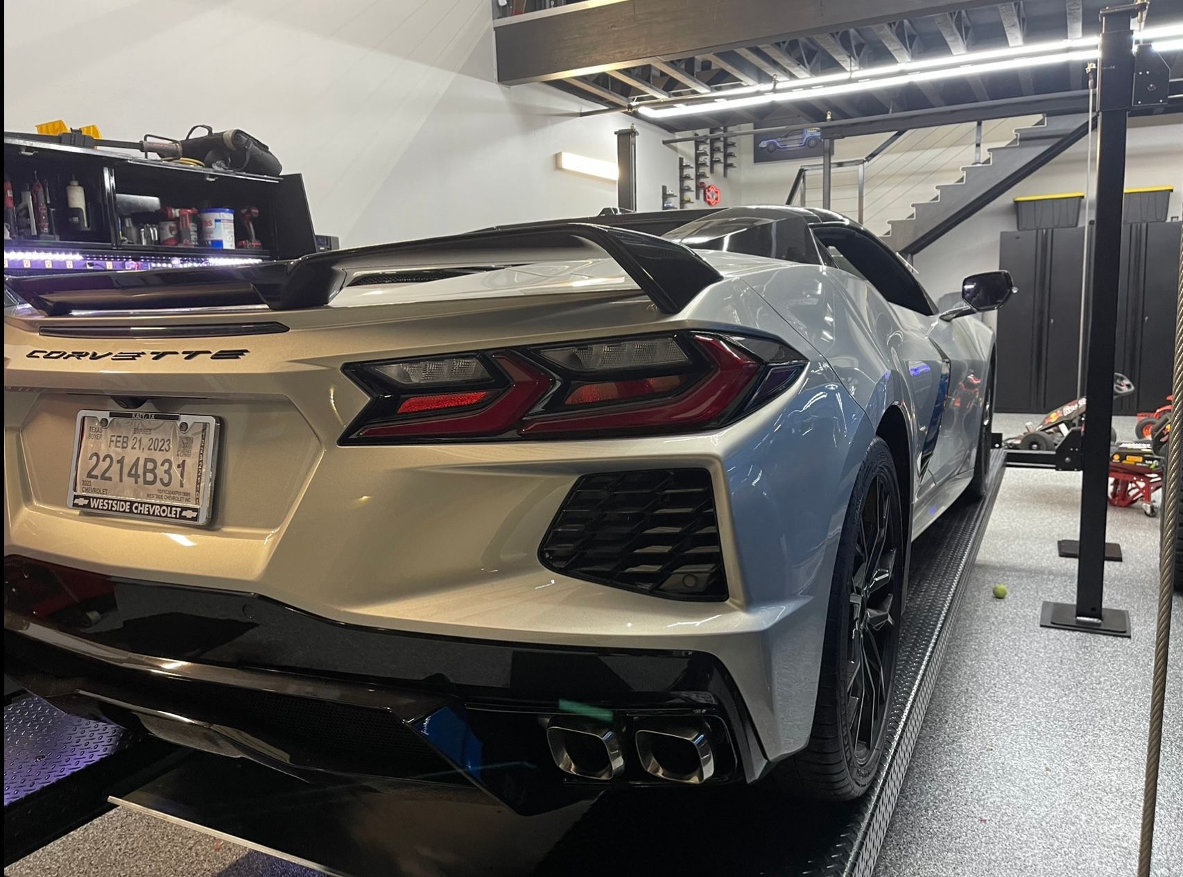 White Corvette sports car on a lift inside a garage; license plate visible. | Auto Motive