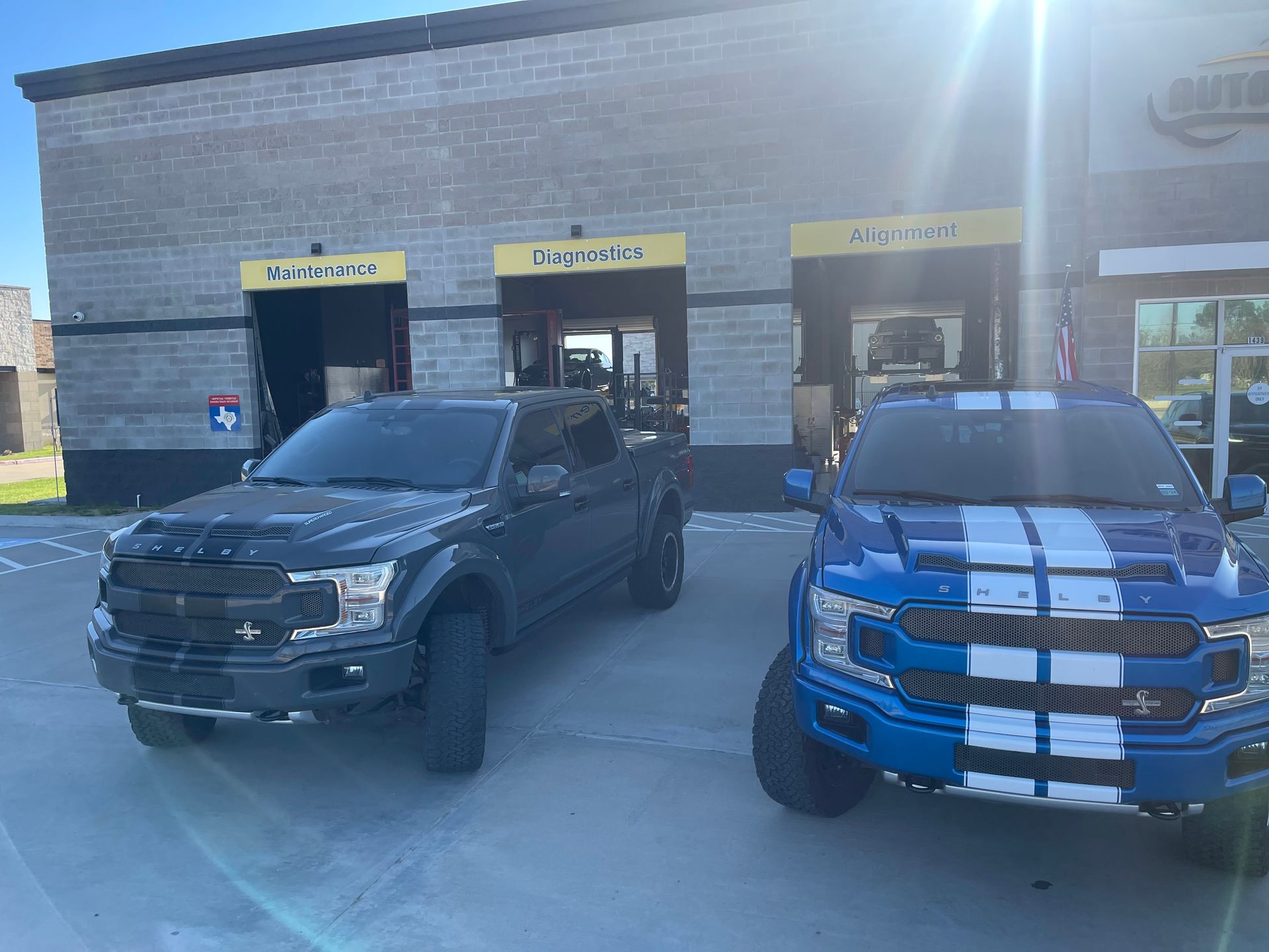 Two modified Ford trucks parked in front of a business on a sunny day. | Auto Motive
