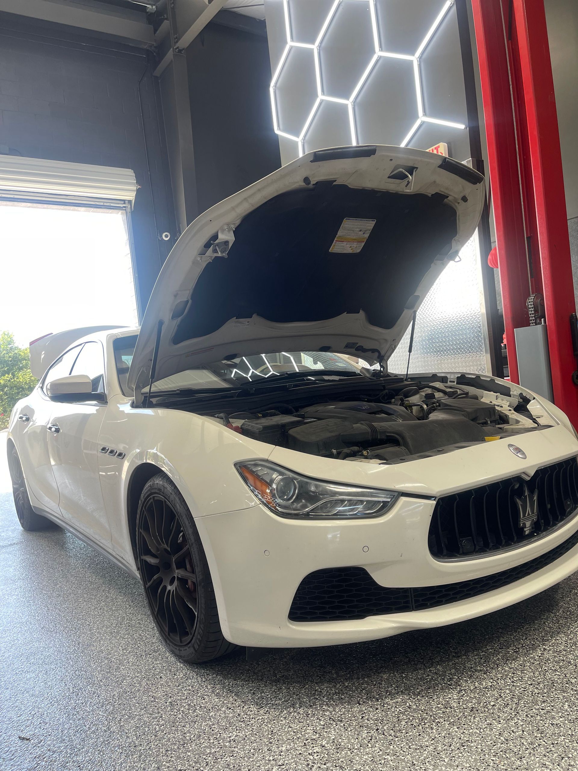 White Maserati with open hood in a garage, black wheels, bright lights. | Auto Motive