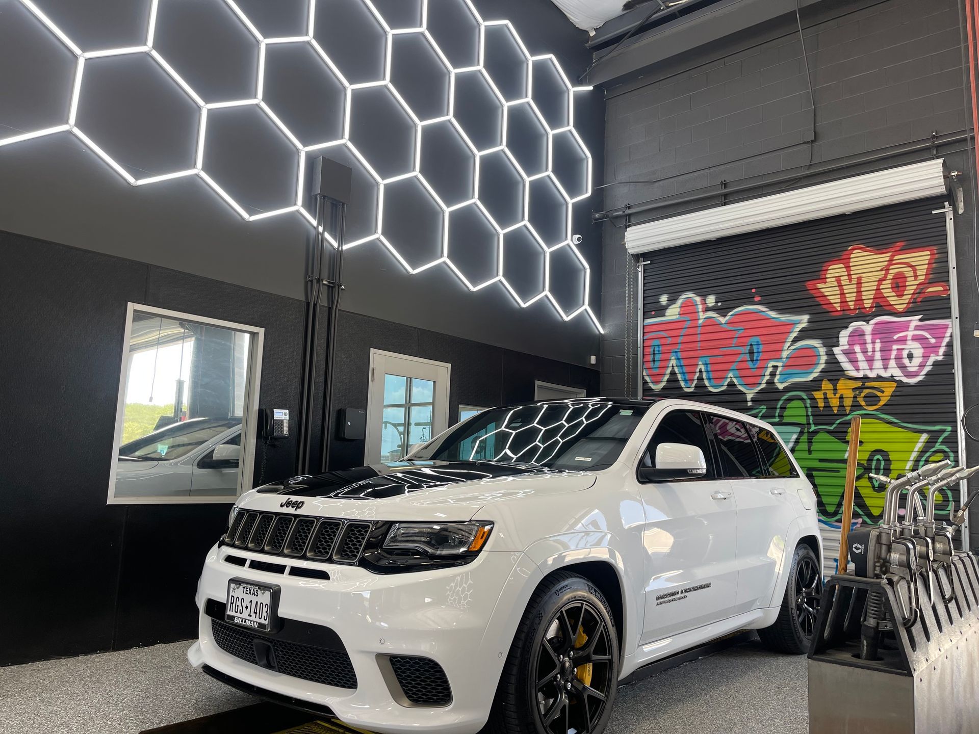 White SUV parked inside a garage with hexagon-shaped lights on the ceiling and graffiti art on a roll-up door. | Auto Motive