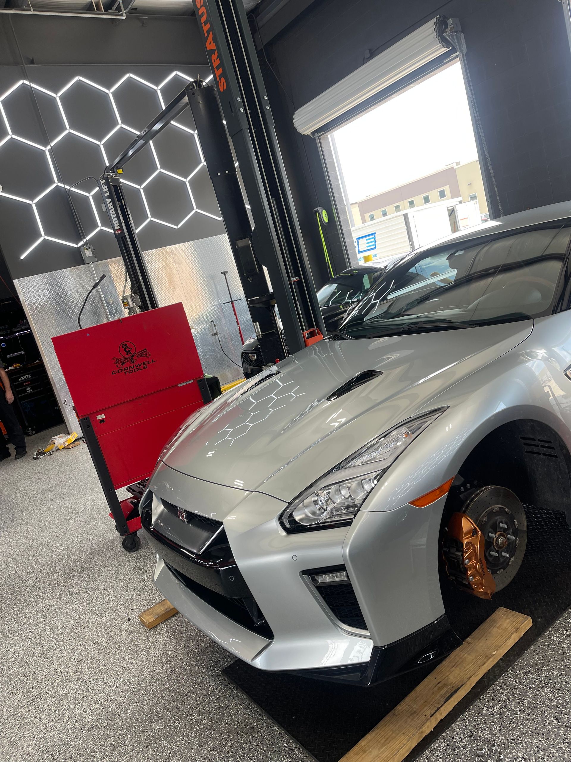 Silver sports car on a lift in a garage, with orange brake calipers and a red toolbox nearby. | Auto Motive