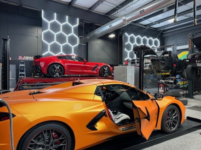 Orange and red sports cars in a garage with hexagon-shaped wall lights; door open on orange car. | Auto Motive