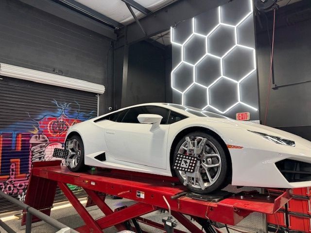 White Lamborghini being aligned on a red lift in a garage with honeycomb-shaped wall lights.