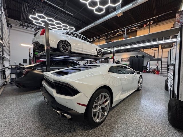 White Lamborghini in a garage with a white car on a lift above it.