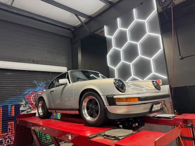Silver Porsche 911 on a red lift in a garage, illuminated by a honeycomb wall light.