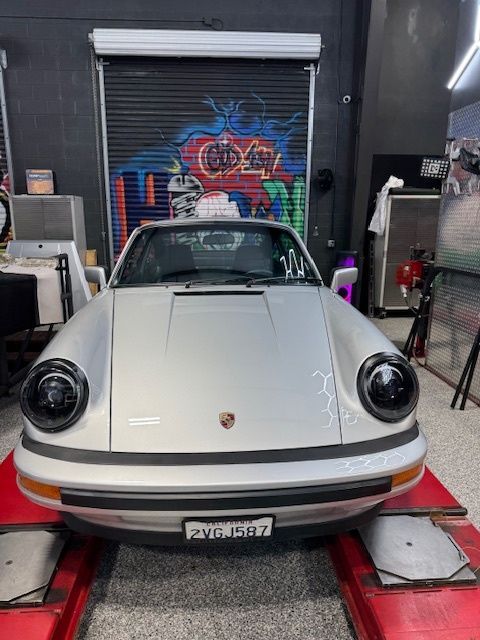 Silver Porsche 911 on a lift, in a garage, with blacked-out headlights.