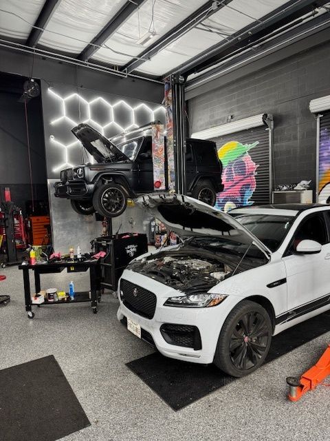 A car repair shop with a white Jaguar and a black SUV on a lift.