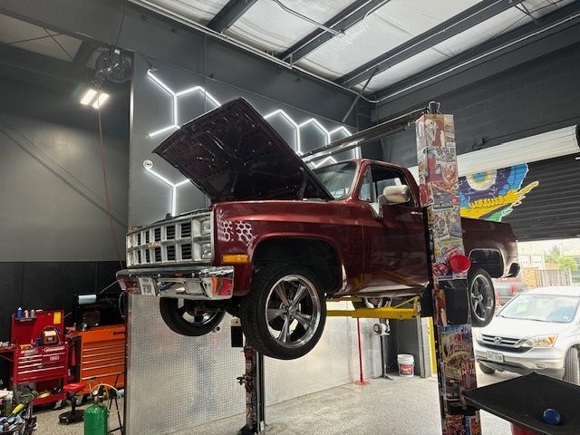 Maroon pickup truck on a lift in a garage with tools, and neon hexagon decor on the wall. | Auto Motive