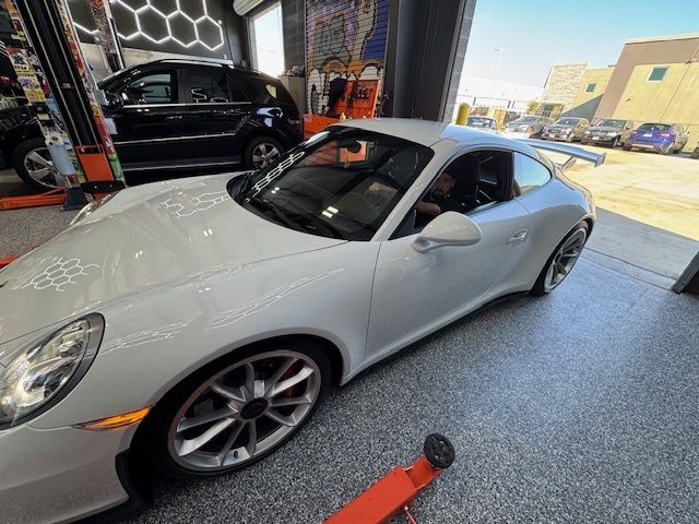 White Porsche sports car inside a shop with an open door, another car in the background.