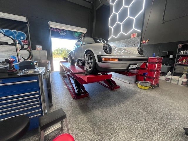 Silver Porsche on a red lift inside a garage with a honeycomb-shaped light.