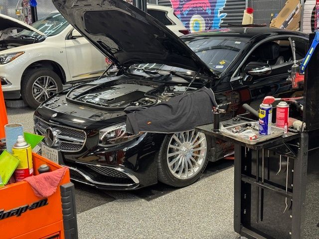 Black Mercedes sedan with open hood in a garage, tools visible.