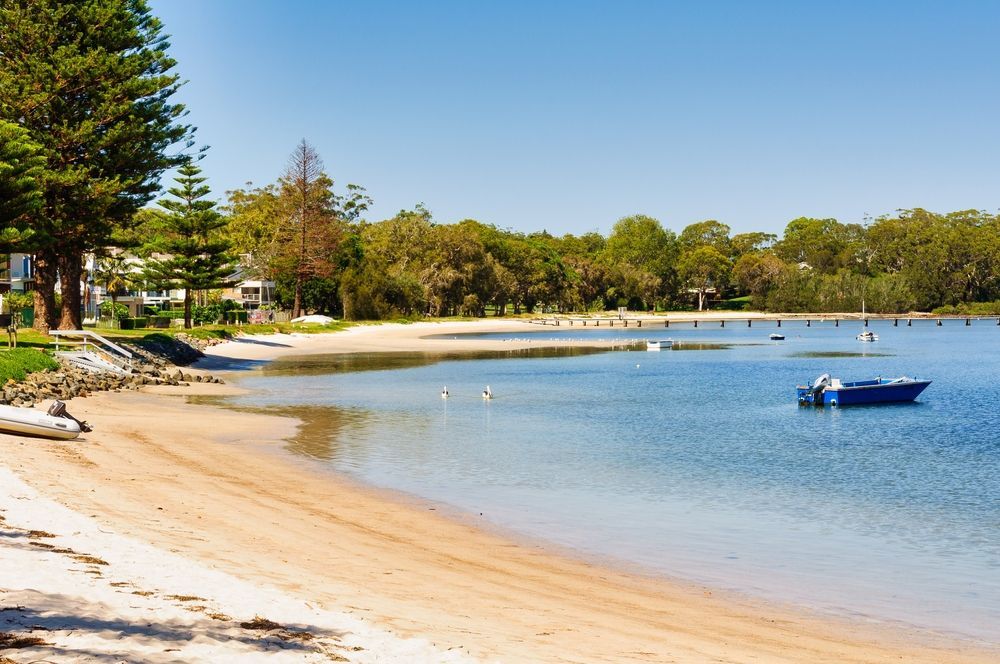 A Boat is Floating on the Water Near a Beach — Port Stephens Removals & Storage In Soldiers Point, NSW