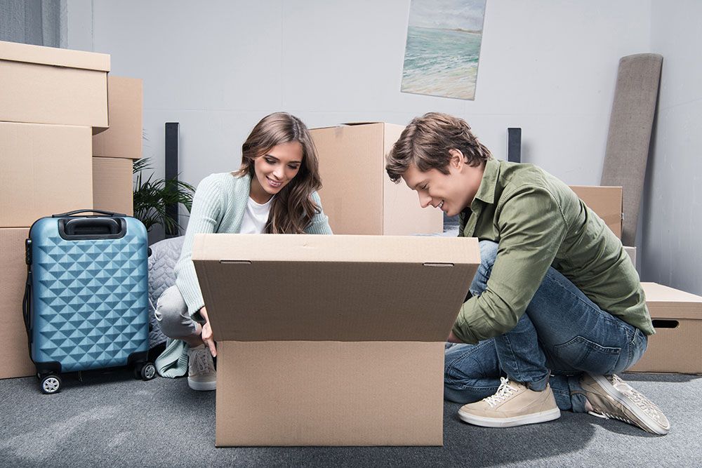 A Man and a Woman Are Opening a Cardboard Box in a Living Room — Port Stephens Removals & Storage In Salt Ash, NSW