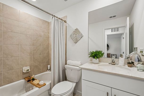 Bright bathroom with white vanity, mirror, toilet, bathtub, and floral shower curtain