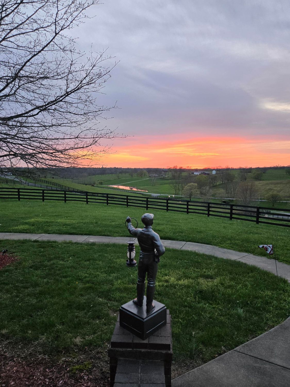 A statue of a man holding a lantern in front of a sunset.