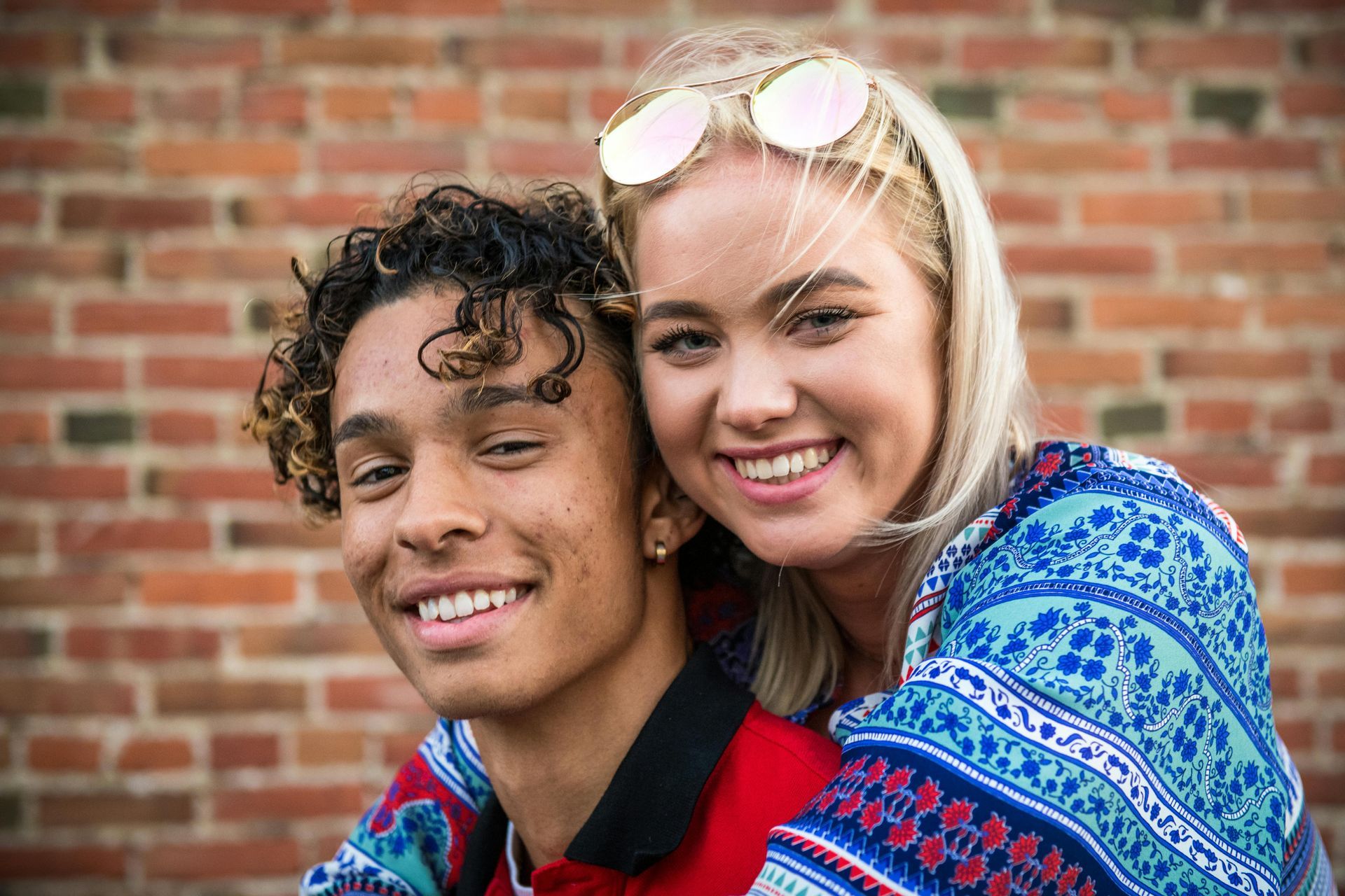 A man and a woman are posing for a picture in front of a brick wall.