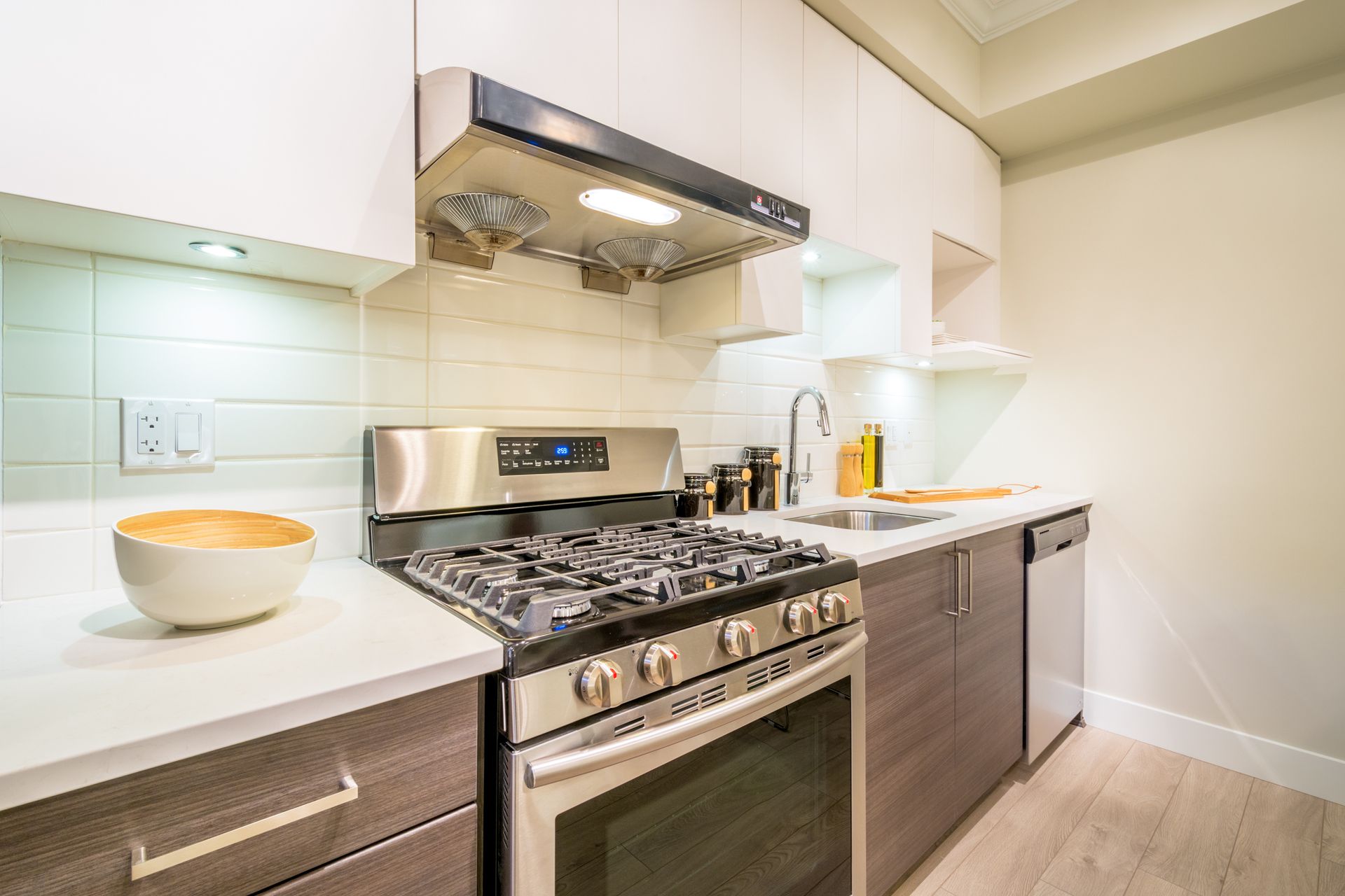 Modern kitchen with stainless steel stove, white countertops, dark cabinets, and white backsplash.