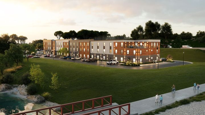 Multi-story apartment building on a grassy hill near a pond and path, with cars parked out front.