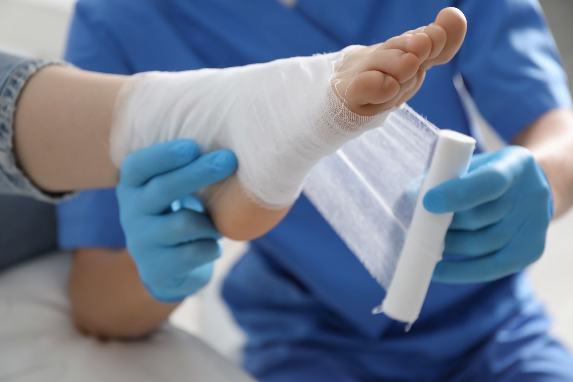 Gloved hands wrapping a white bandage around a patient’s foot in a medical setting
