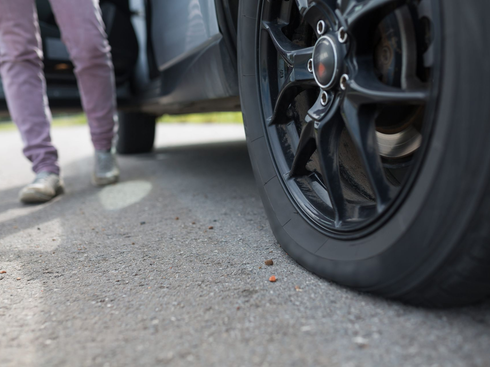 Person standing beside a black car with a flat tire on a roadside.