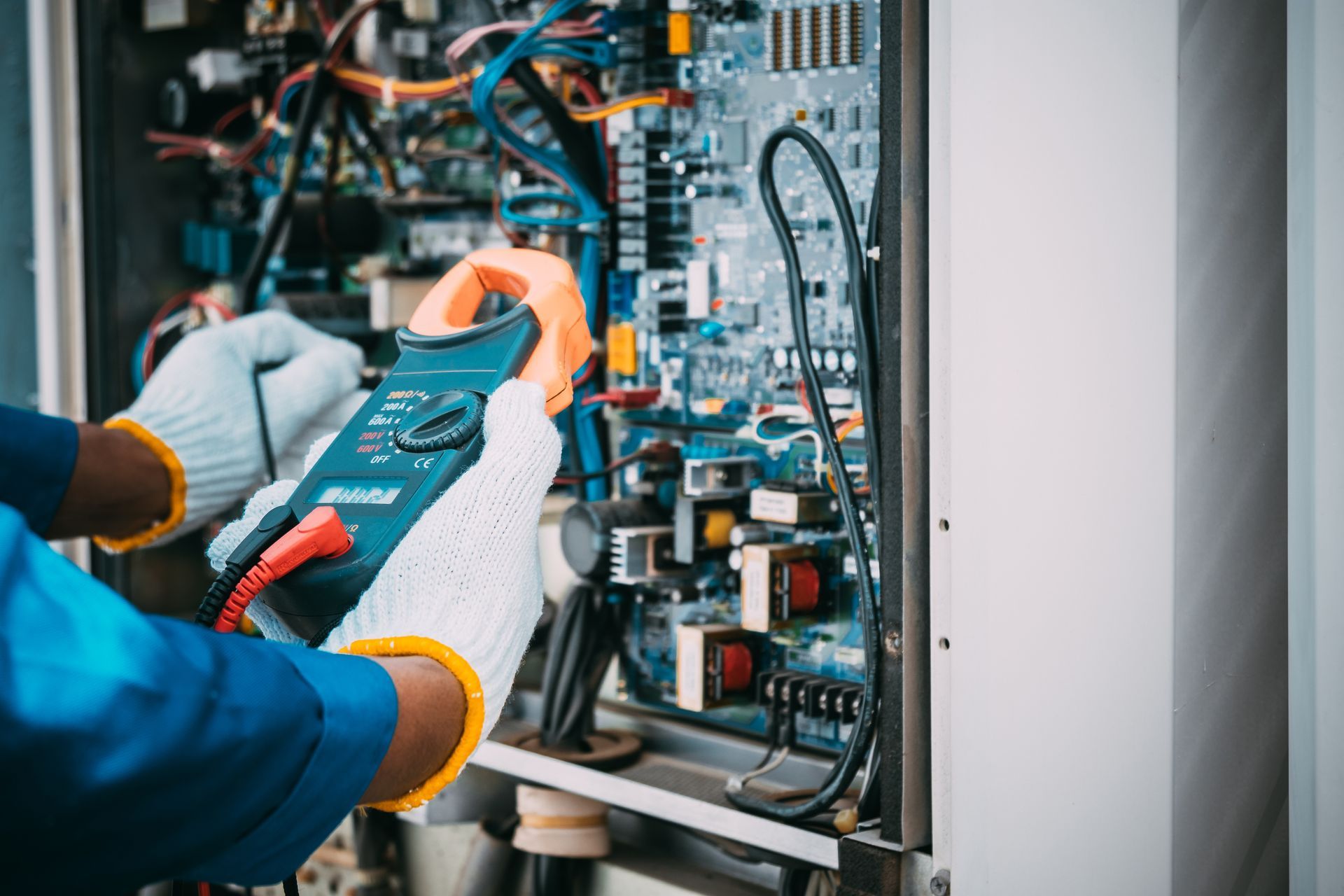 Technician in blue shirt and gloves using a clamp meter to diagnose electrical equipment.