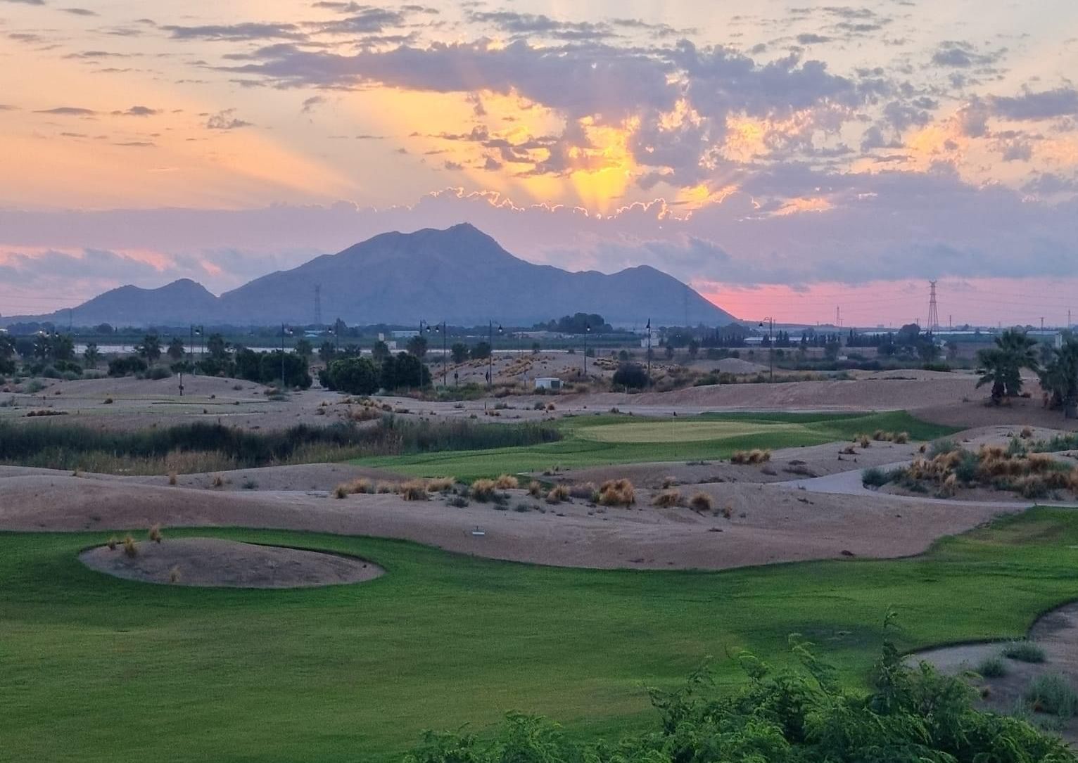 A view of a golf course at sunset with mountains in the background.