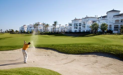A man is hitting a golf ball out of a bunker on a golf course.