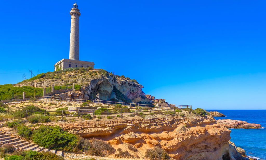A lighthouse is sitting on top of a rocky hill next to the ocean.