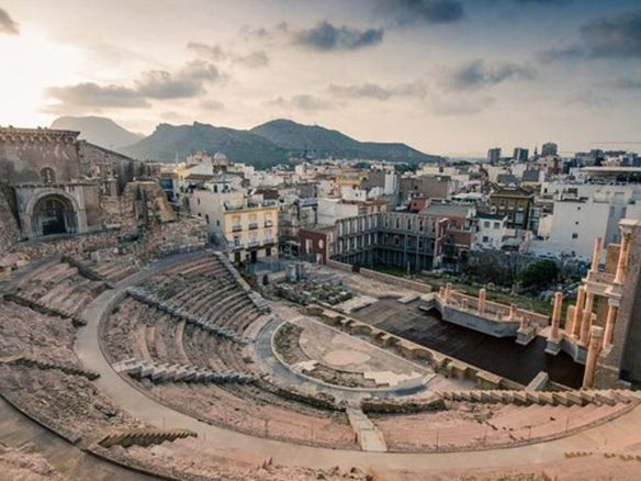 An aerial view of an ancient amphitheater with a city in the background.