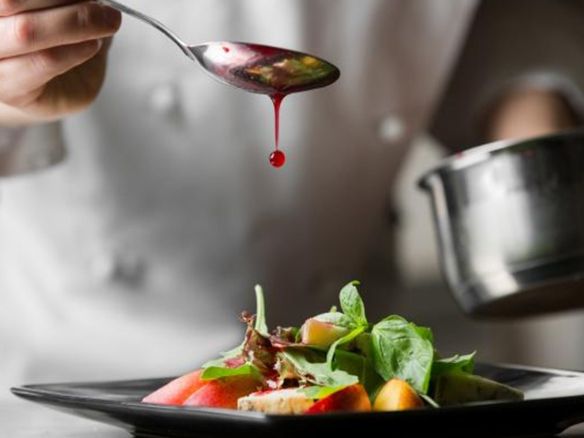 A chef is pouring sauce on a salad with a spoon