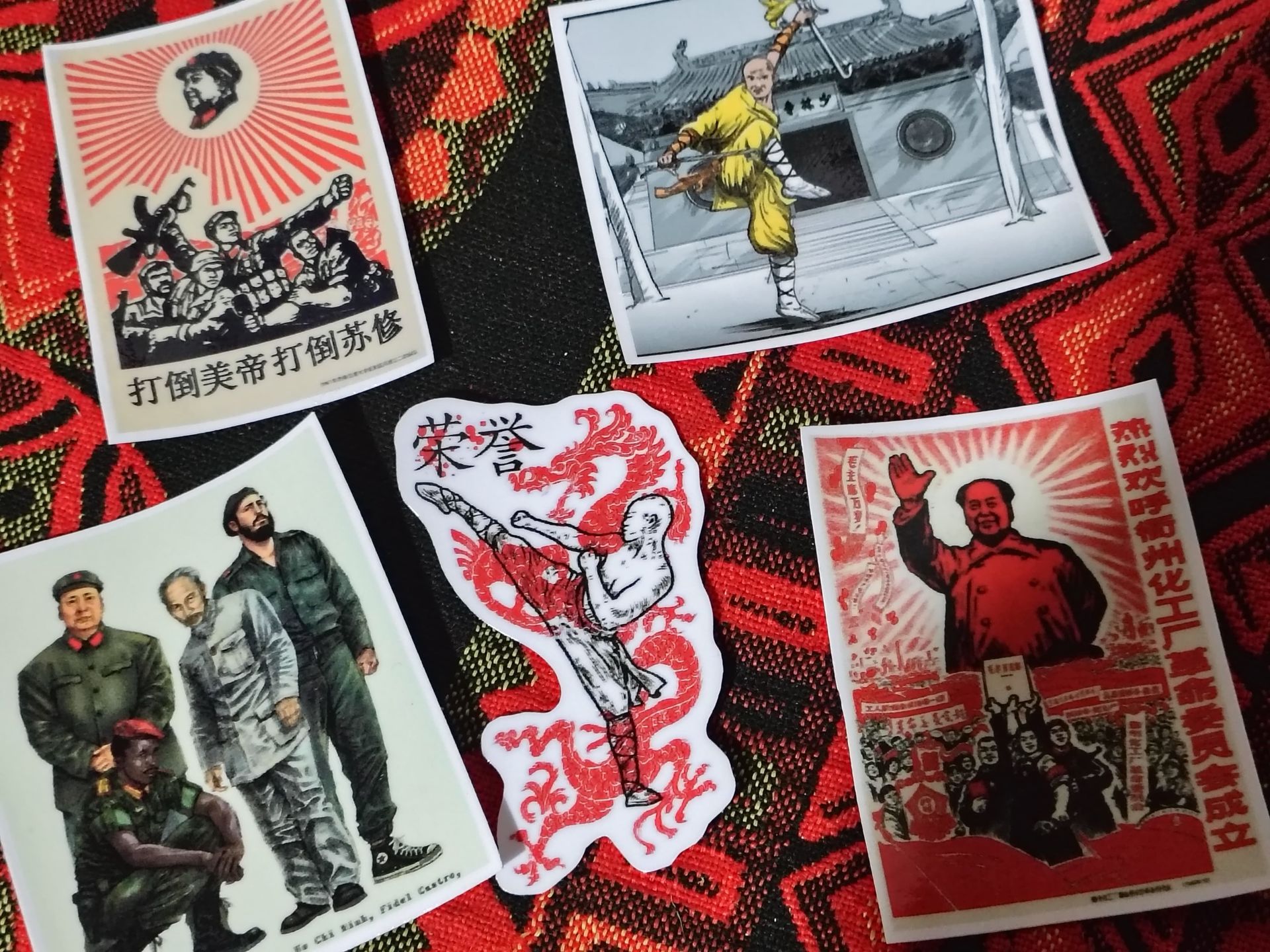 Cinco pegatinas con temática política y de artes marciales dispuestas sobre un fondo de tela roja estampada.