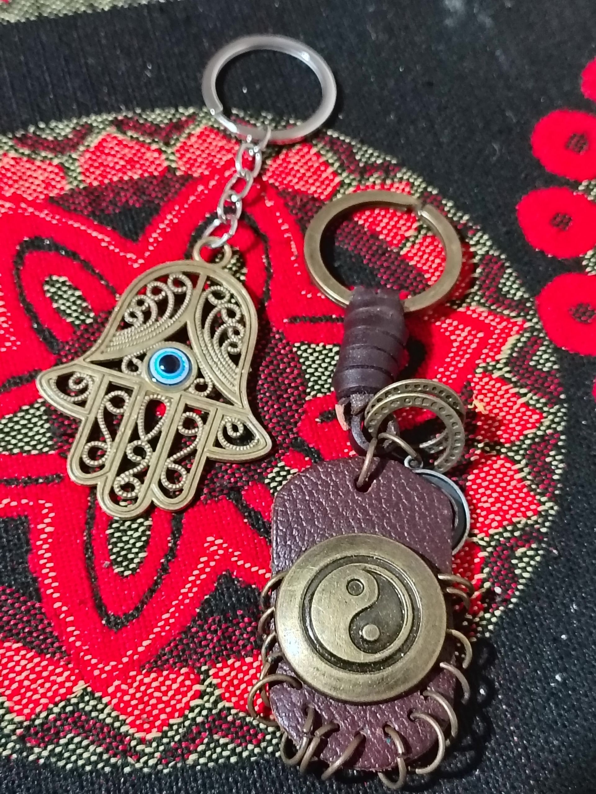 Dos llaveros de metal, uno con una mano de Hamsa de filigrana con un ojo azul, y el otro con un símbolo yin-yang