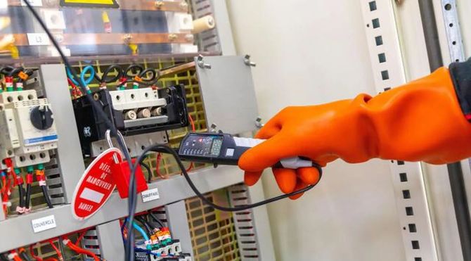Gloved hand using a thermal camera to inspect electrical control panels in a workshop