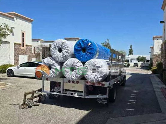 Truck loaded with large rolled materials in white, blue, gray, and orange parked on a residential street