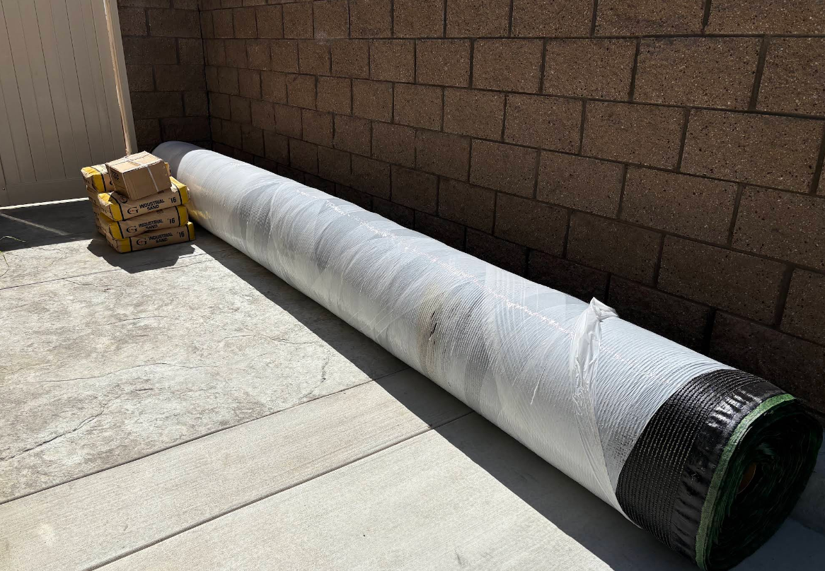 Long silver duct or pipe lying on a concrete patio beside a brick wall, with a small box at one end