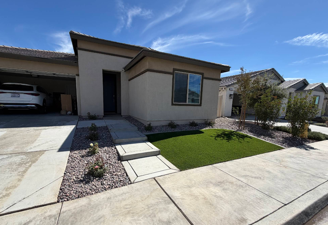 Modern single-story house with beige exterior, driveway, green lawn, and blue sky