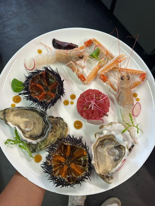 Ostriche crude assortite e altri frutti di mare presentati con cura su un piatto bianco, accompagnati da salse e guarnizioni.