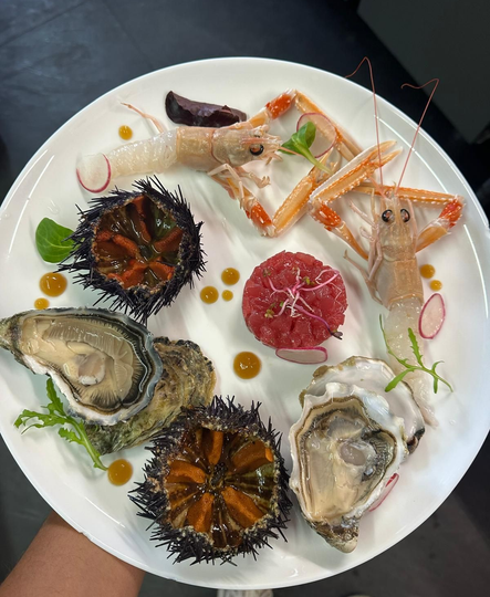 Frutti di mare crudi assortiti su un piatto bianco: ostriche, ricci di mare, gamberi e agrumi a fette.