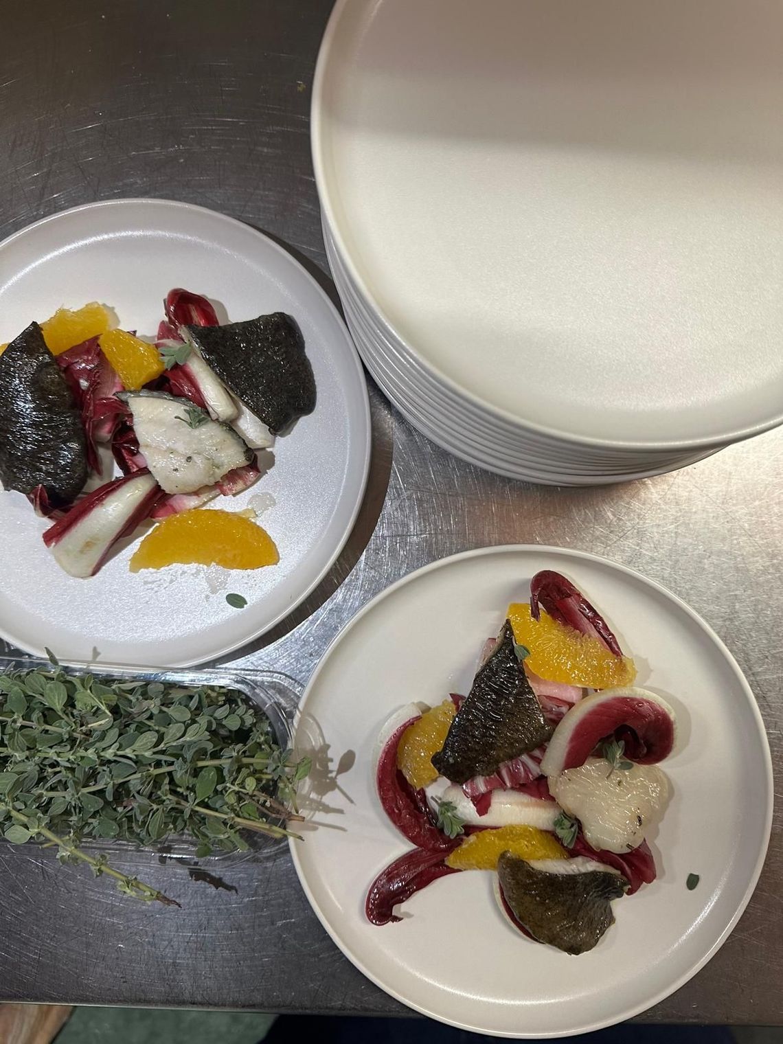 Due ciotole di dessert con frutta ed erbe aromatiche accanto a una tazza bianca su un tavolo di metallo.
